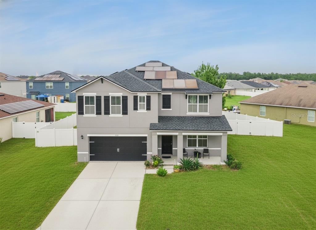 A two-story suburban house with a gray exterior, black garage door, and rooftop solar panels — 6115 GREY HERON DRIVE, WINTER HAVEN, FL
