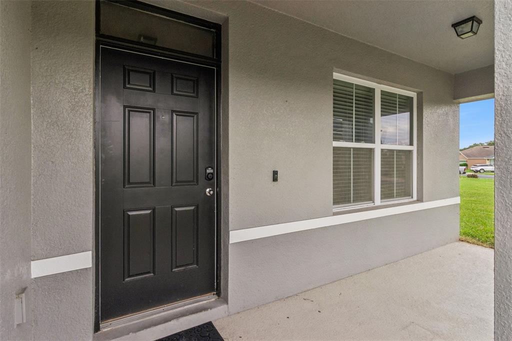 A black front door with a transom window sits beside a window on a porch — 6115 GREY HERON DRIVE, WINTER HAVEN, FL