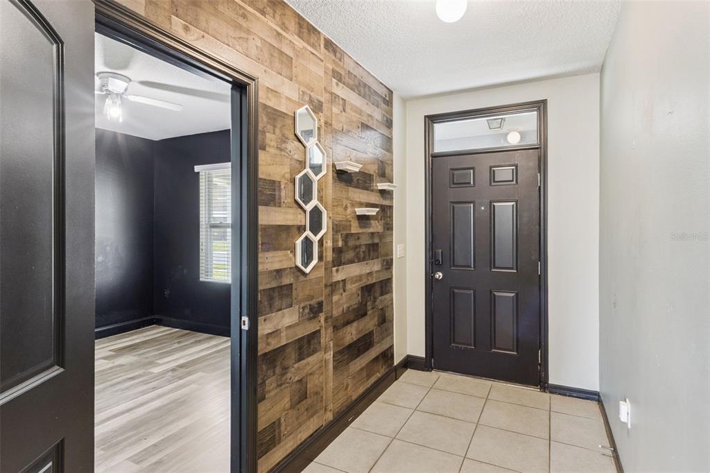 An entryway features a wood-paneled accent wall, a black front door, and tiled flooring — 6115 GREY HERON DRIVE, WINTER HAVEN, FL