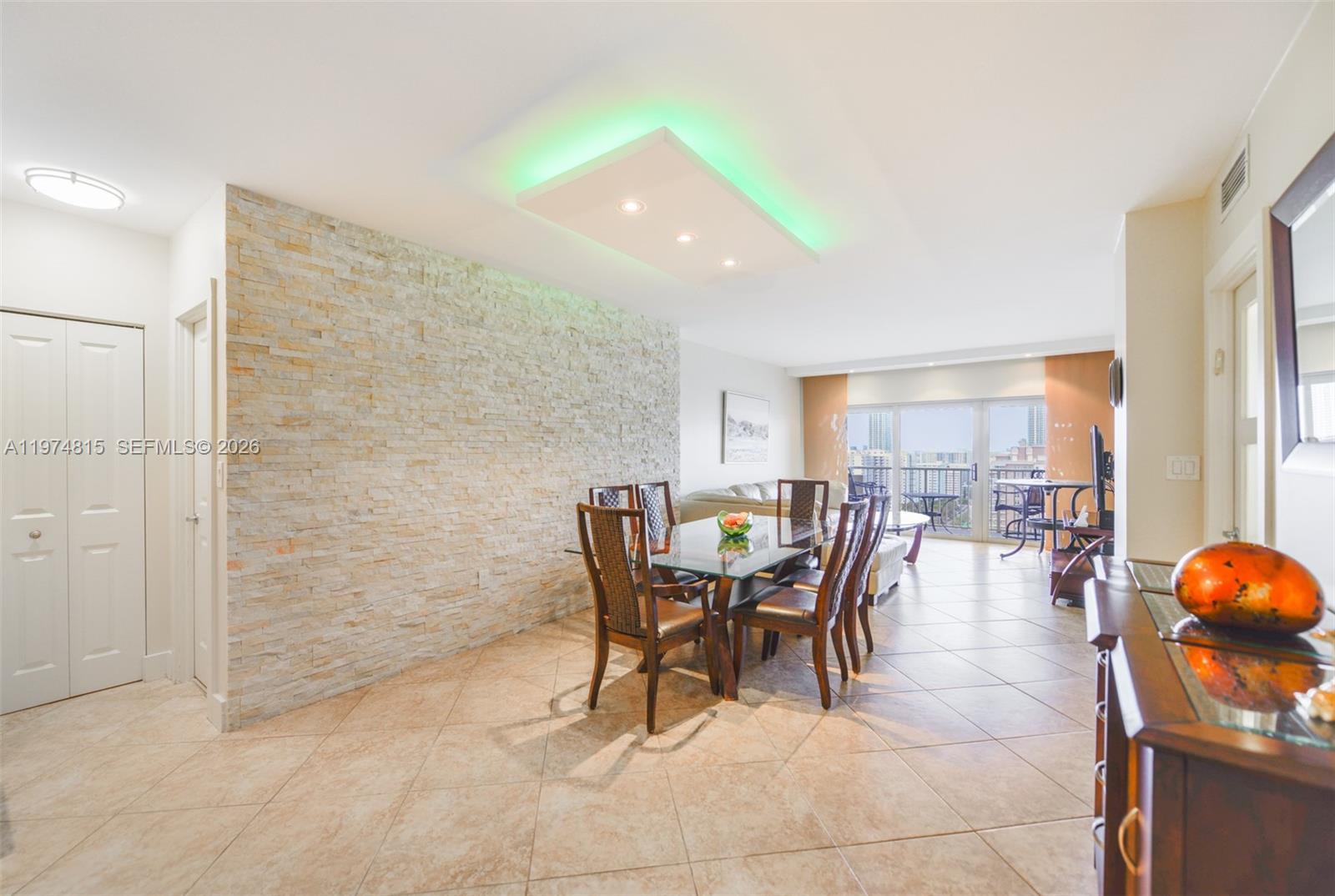 A dining area features a stone accent wall, a glass table, and green ceiling lighting — 1980 S Ocean Dr # 21M, Hallandale Beach FL 33009, HALLANDALE BEACH, FL