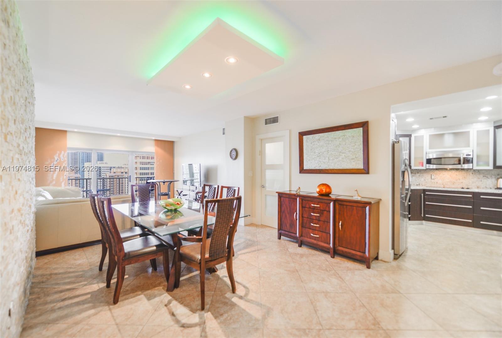 A dining area features a glass table, wooden chairs, and a modern green-lit ceiling fixture — 1980 S Ocean Dr # 21M, Hallandale Beach FL 33009, HALLANDALE BEACH, FL