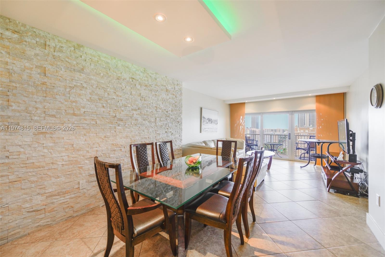 A dining area with a glass table and stone wall features a view of city buildings — 1980 S Ocean Dr # 21M, Hallandale Beach FL 33009, HALLANDALE BEACH, FL