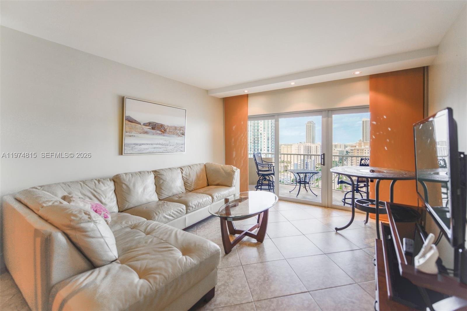 A living room features a beige sectional sofa, glass coffee table, and a balcony with city views — 1980 S Ocean Dr # 21M, Hallandale Beach FL 33009, HALLANDALE BEACH, FL