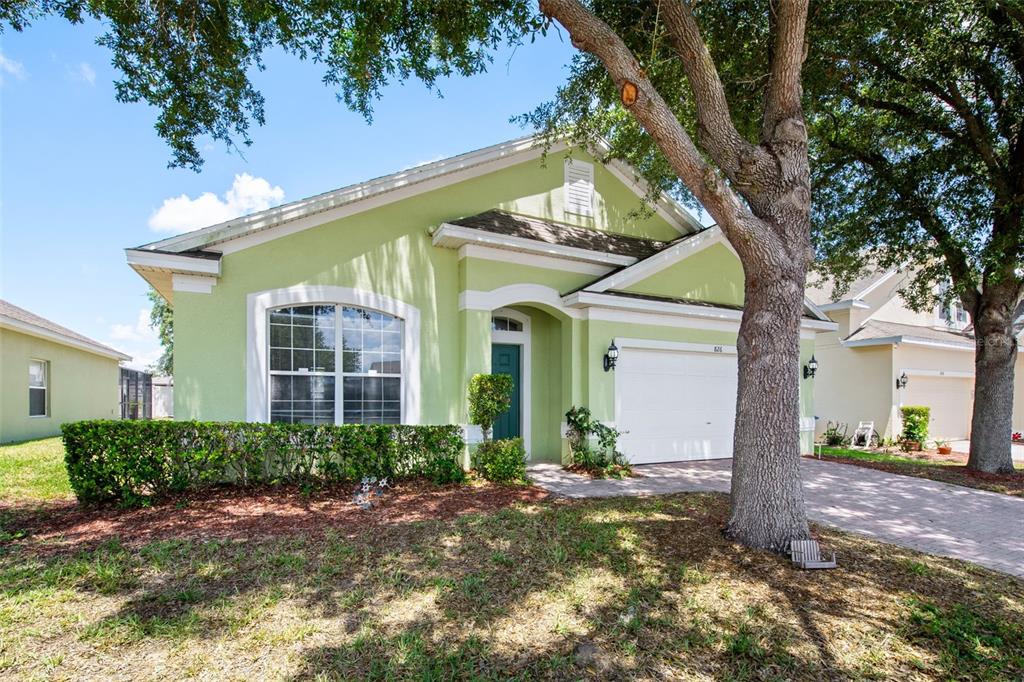 A light green single-story house with a white garage and a large tree in front — 826 ANDALUSIA LOOP, DAVENPORT, FL