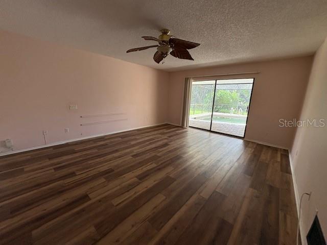 An empty living room features wood-look flooring, a ceiling fan, and sliding glass doors to a pool — 4240 CHARING CROSS ROAD, SARASOTA, FL