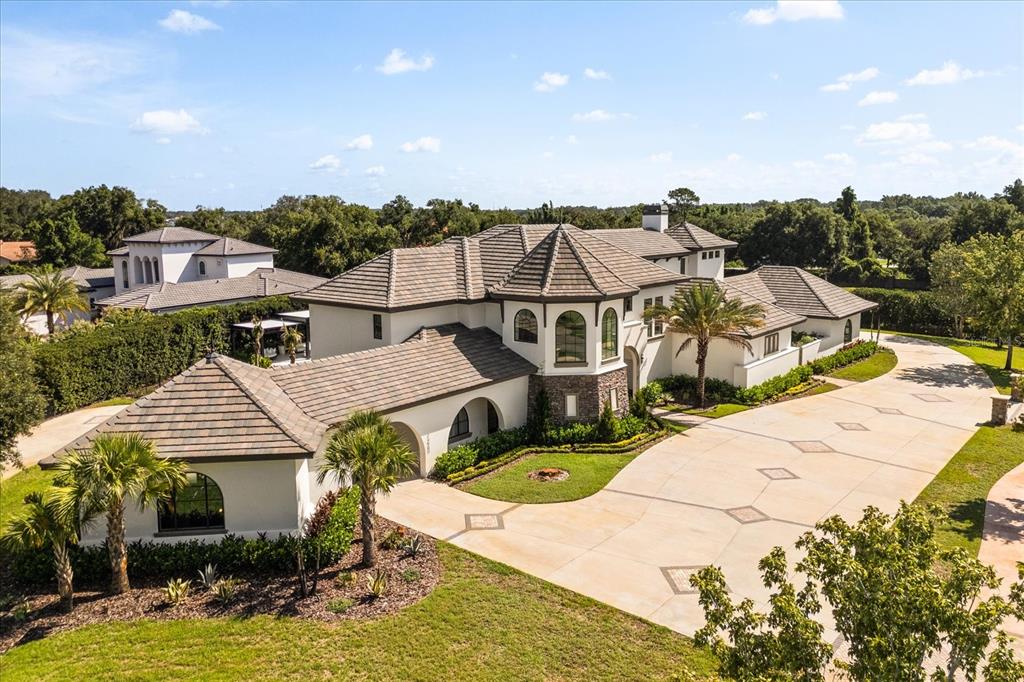 An aerial view of a large, multi-roofed luxury home with a spacious concrete driveway — 12237 PARK AVENUE, WINDERMERE, FL
