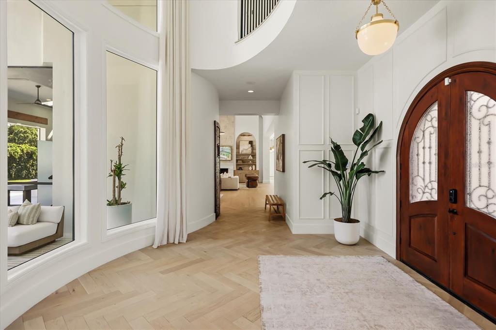A bright foyer features herringbone wood floors, a large arched wooden door, and a plant — 12237 PARK AVENUE, WINDERMERE, FL