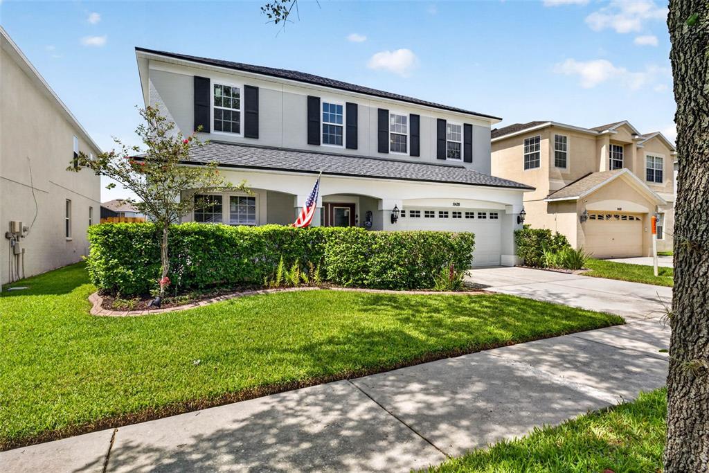 A two-story suburban house features a front hedge, a driveway, and an American flag — 11428 BLUE LILAC AVENUE, RIVERVIEW, FL