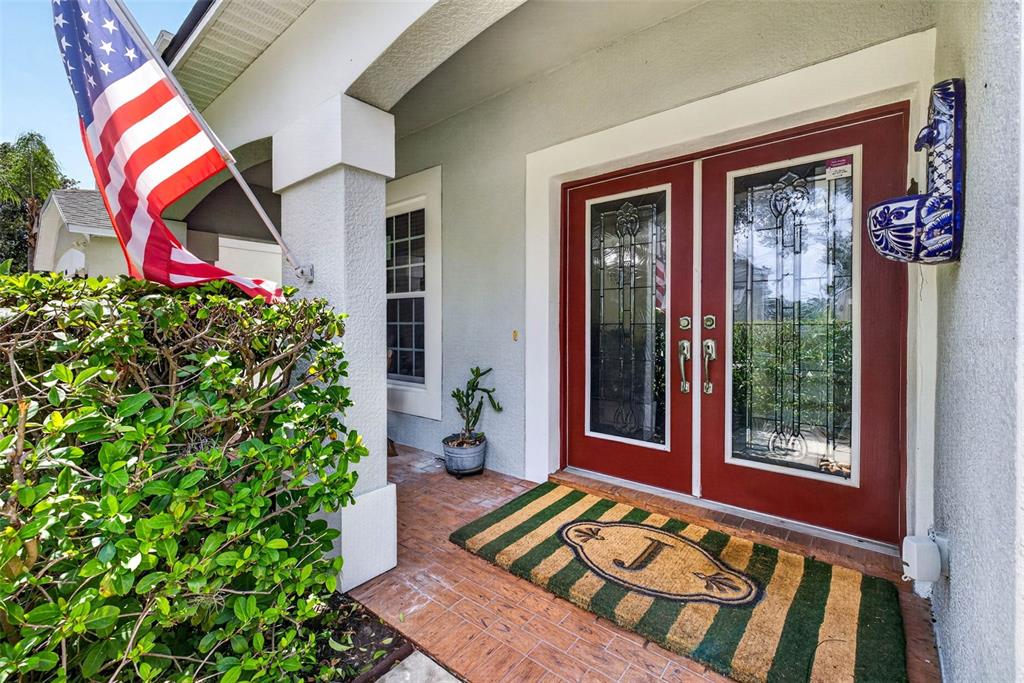 A front porch features a red double door, a striped doormat, and an American flag — 11428 BLUE LILAC AVENUE, RIVERVIEW, FL
