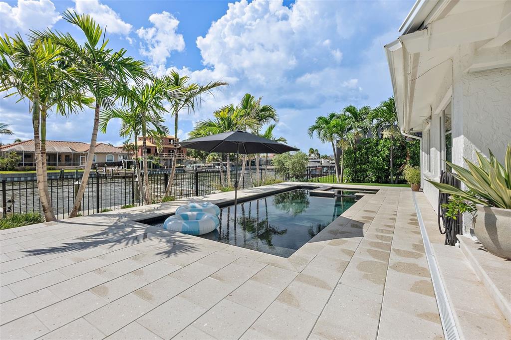 A rectangular swimming pool sits on a stone patio beside a house with palm trees — 1985 CAROLINA AVENUE NE, ST PETERSBURG, FL