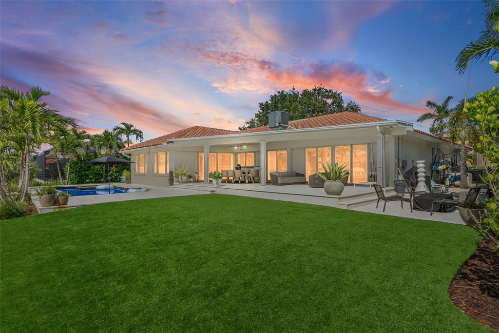 A backyard with a green lawn, a swimming pool, and a covered patio of a house — 1985 CAROLINA AVENUE NE, ST PETERSBURG, FL