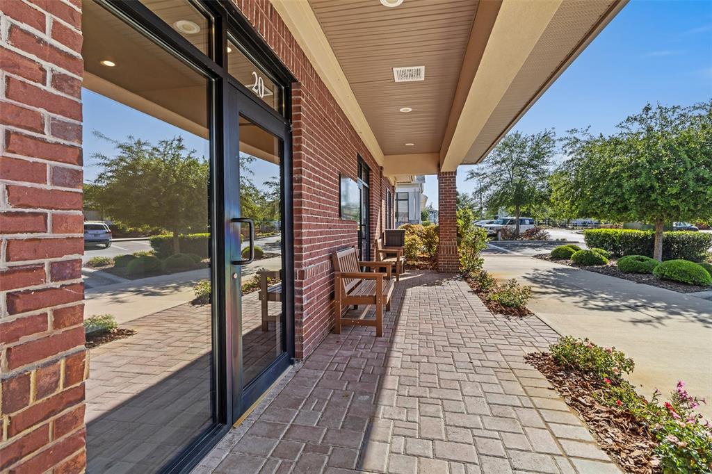 A brick building exterior features a glass door, a covered walkway, and wooden benches — 13577 NW 2ND LANE UNIT 20, NEWBERRY, FL