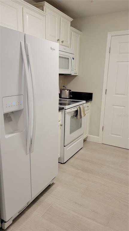 A kitchen features white appliances, white cabinetry, black countertops, and light-colored tile flooring — 750 N TAMIAMI TRAIL UNIT 418, SARASOTA, FL