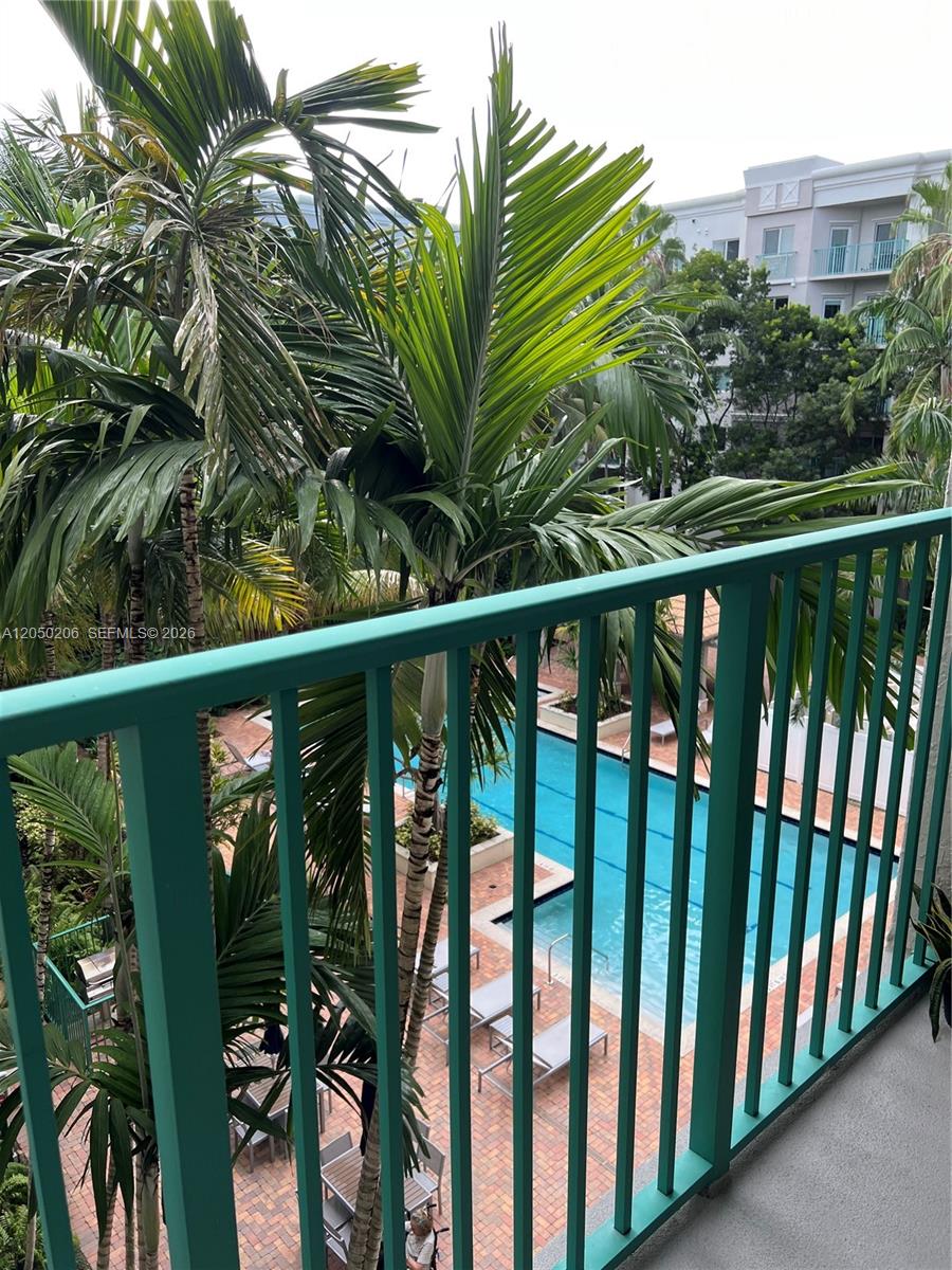 A balcony with a green railing overlooks a swimming pool surrounded by palm trees — 6001 SW 70th St # 421, South Miami FL 33143, SOUTH MIAMI, FL
