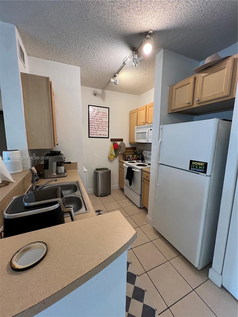 A galley-style kitchen features light wood cabinets, white appliances, and beige tile flooring — 6001 SW 70th St # 421, South Miami FL 33143, SOUTH MIAMI, FL