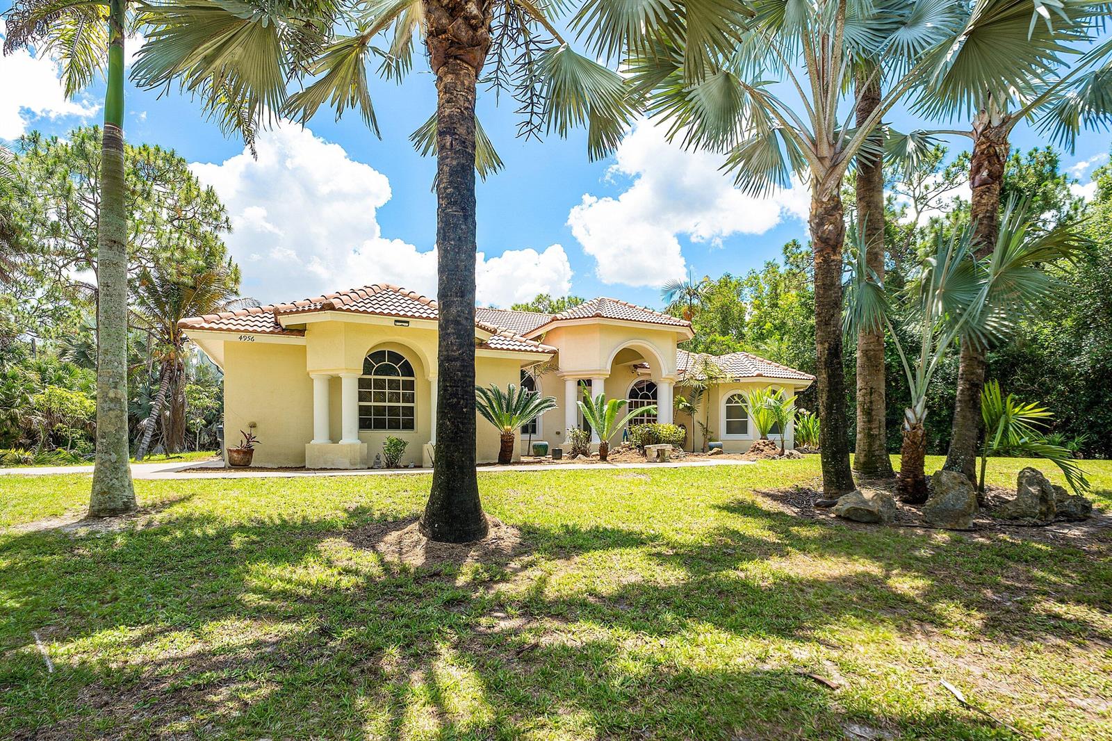 A single-story yellow stucco house with a tiled roof sits behind several tall palm trees — 4956 200th Trail N, Loxahatchee FL 33470, LOXAHATCHEE, FL
