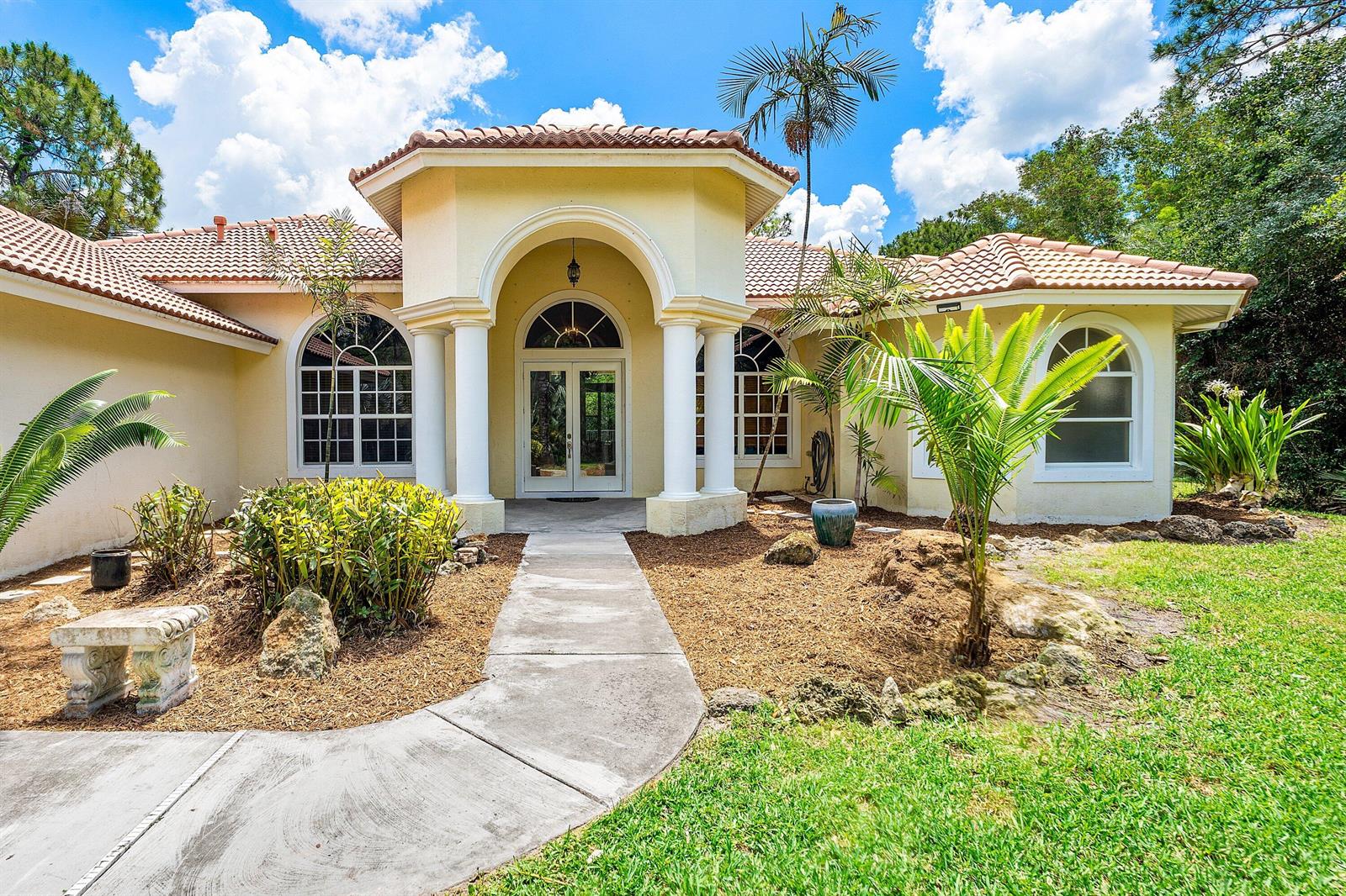 A single-story house with a yellow stucco exterior, arched entryway, white columns, and tile roof — 4956 200th Trail N, Loxahatchee FL 33470, LOXAHATCHEE, FL