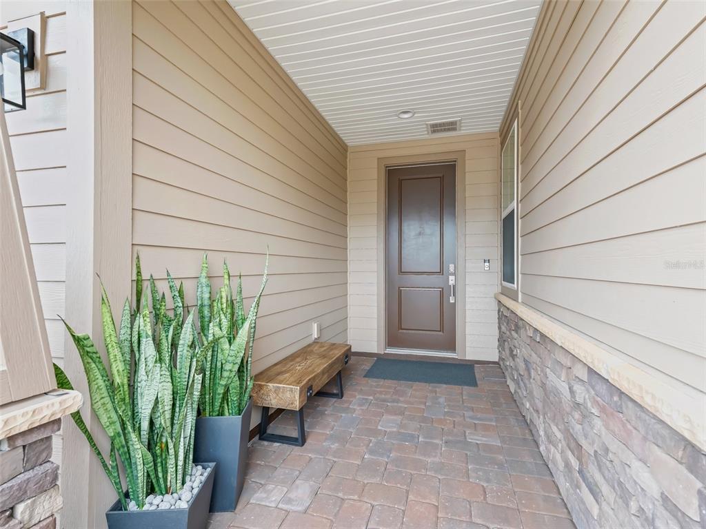A covered entryway features tan siding, stone accents, a wooden bench, and a brown door — 5672 NW 40TH PLACE, OCALA, FL