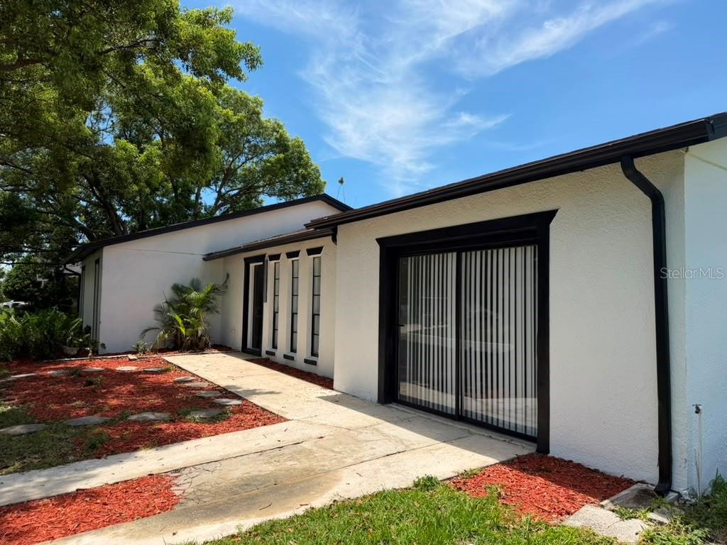 A white house exterior features a concrete walkway, black window frames, and red mulch landscaping — 144 HIDALGO AVENUE, KISSIMMEE, FL