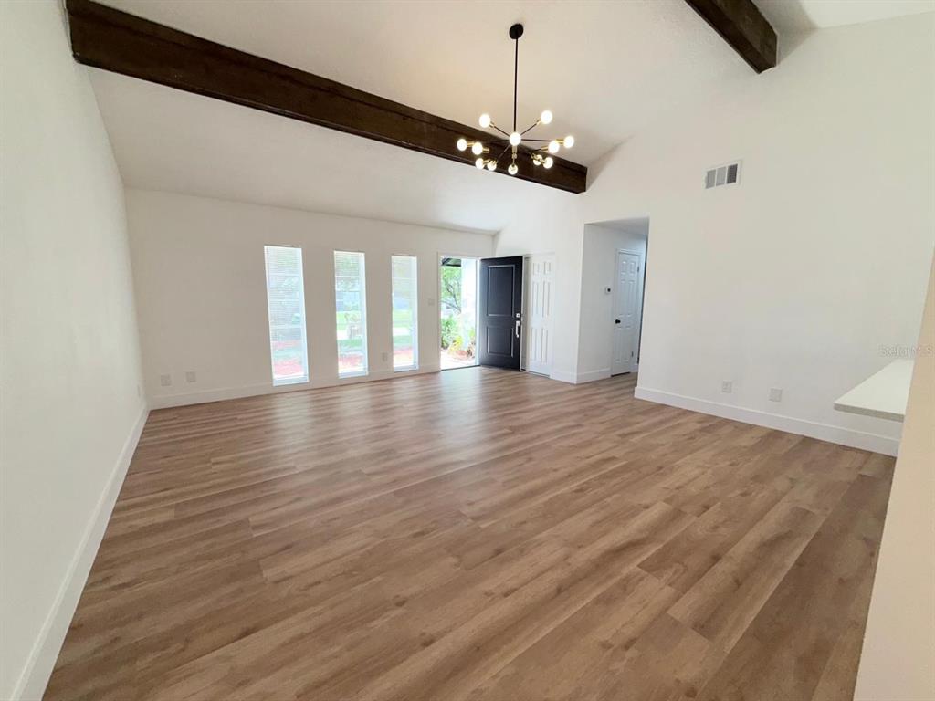 A living room features wood-look flooring, vaulted ceilings with exposed beams, and a modern chandelier — 144 HIDALGO AVENUE, KISSIMMEE, FL