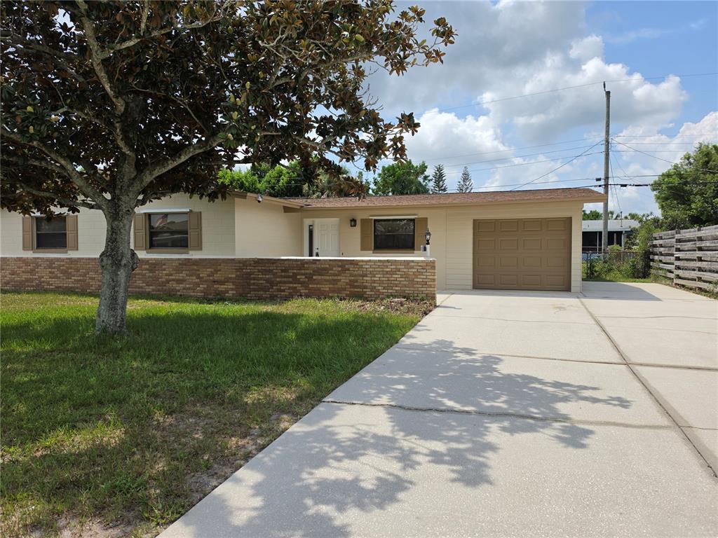 A single-story house with a brick wall, beige siding, a garage, and a large tree — 969 ELKCAM BOULEVARD, COCOA, FL