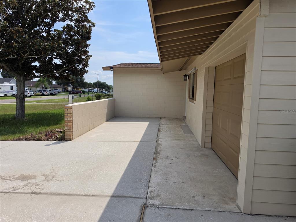 A concrete driveway leads to a garage entrance beside a low masonry wall — 969 ELKCAM BOULEVARD, COCOA, FL