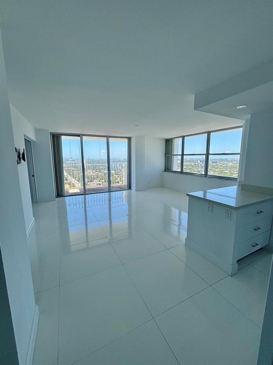 An empty room with white tile floors, a kitchen island, and floor-to-ceiling windows with balcony access — 111 Briny Avenue # 14, Pompano Beach FL 33062, POMPANO BEACH, FL