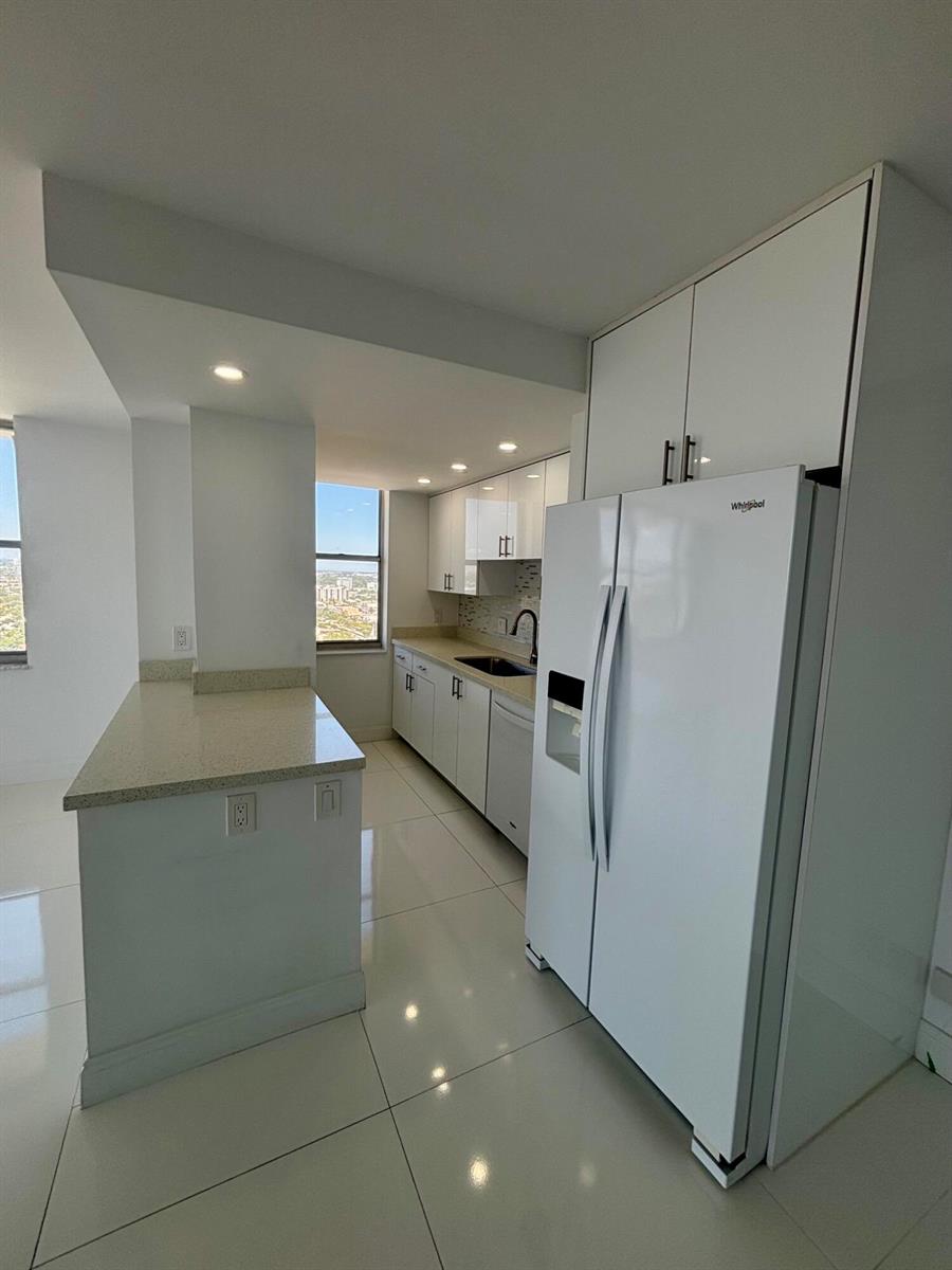 A modern kitchen features white cabinets, light countertops, stainless steel appliances, and tile flooring — 111 Briny Avenue # 14, Pompano Beach FL 33062, POMPANO BEACH, FL