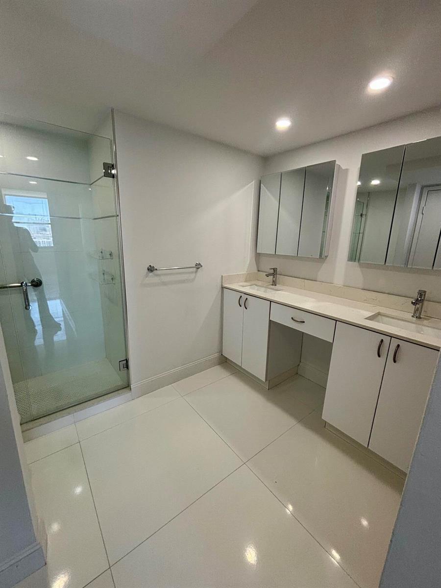 A modern bathroom features a glass-enclosed shower, double vanity with white cabinets, and tiled flooring — 111 Briny Avenue # 14, Pompano Beach FL 33062, POMPANO BEACH, FL
