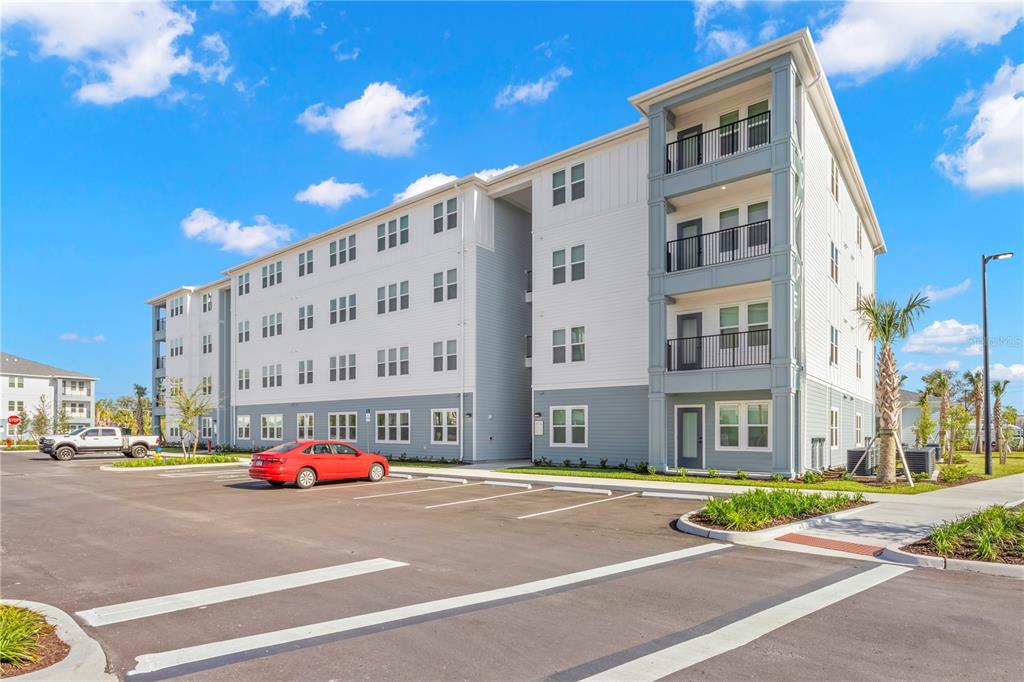 A multi-story apartment building with a parking lot and a red car in front — 9720 BEAMING ROAD UNIT A2, VENICE, FL