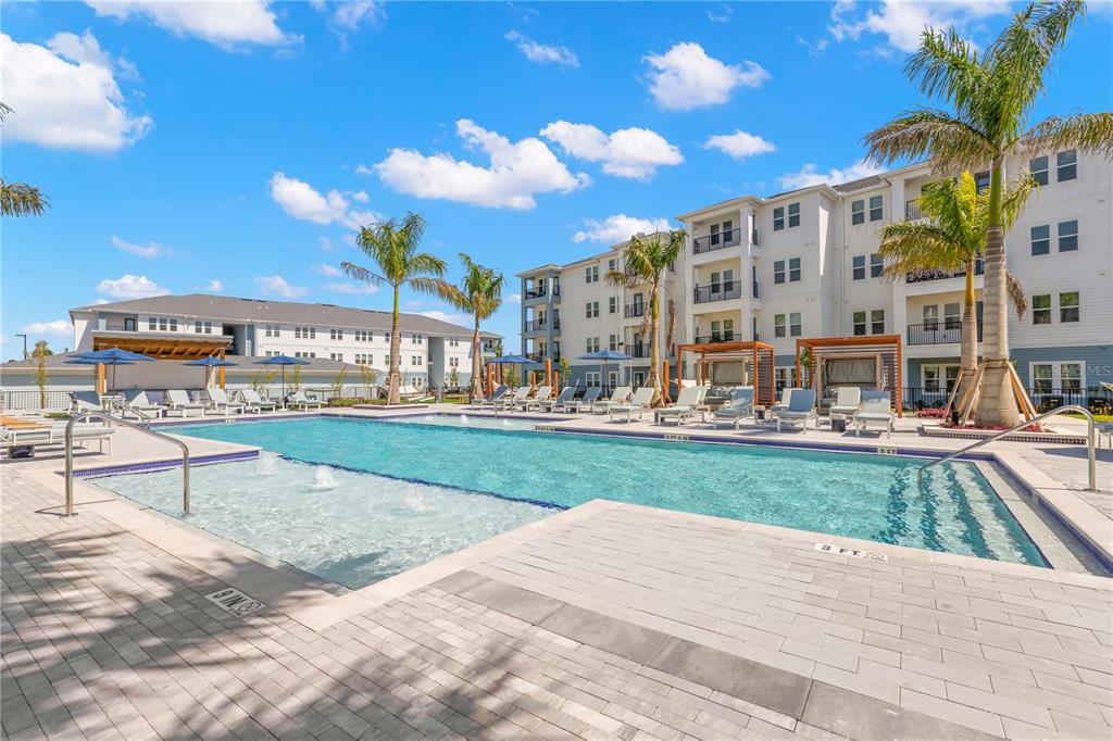 A swimming pool with lounge chairs and cabanas sits in front of a large apartment building — 9720 BEAMING ROAD UNIT A2, VENICE, FL