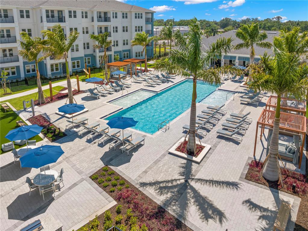 An aerial view of a swimming pool area with lounge chairs, umbrellas, and palm trees — 9720 BEAMING ROAD UNIT A2, VENICE, FL