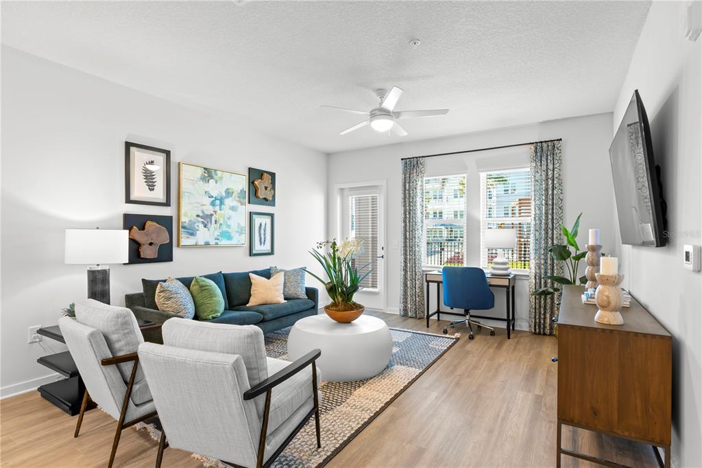 A living room features a blue sofa, two gray armchairs, a desk, and wood flooring — 9720 BEAMING ROAD UNIT A2, VENICE, FL