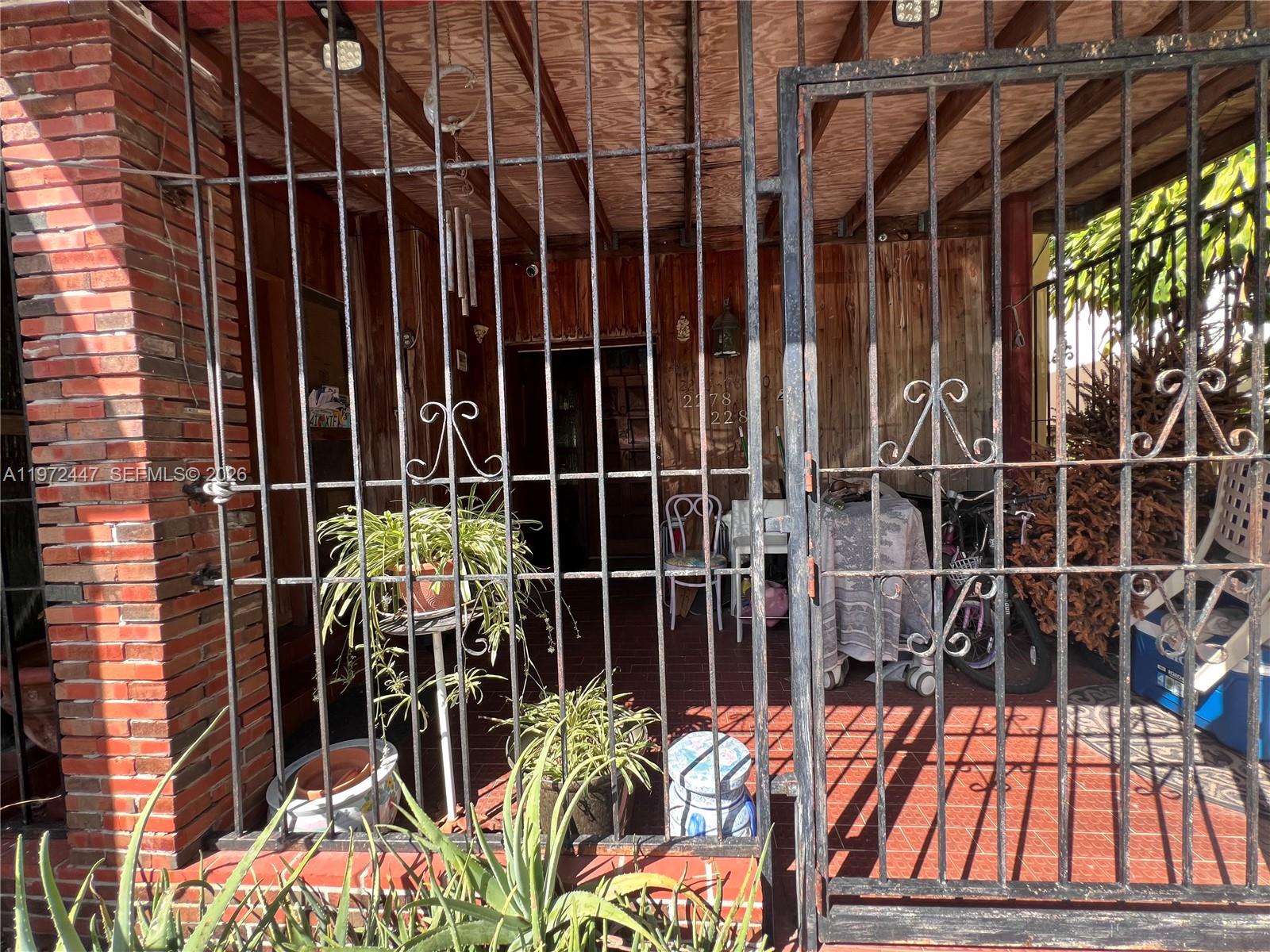 A gated, covered porch features brick flooring, wood-paneled walls, and several potted plants — 2278 SW 16th Ave, Miami FL 33145, MIAMI, FL
