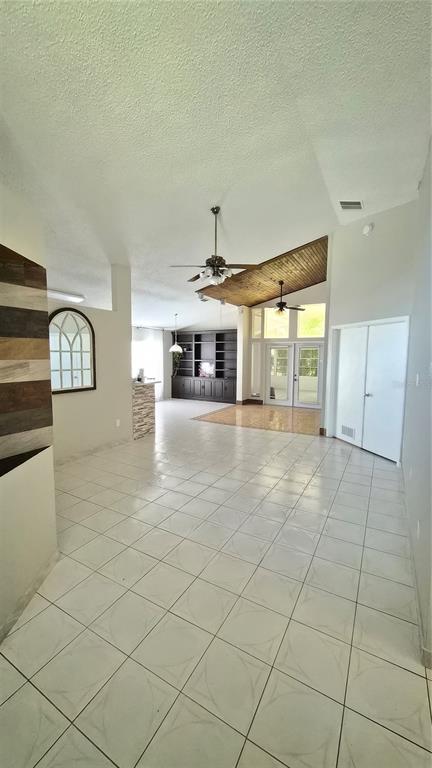 A spacious living area features white tile flooring, a wood-paneled ceiling section, and built-in shelving — 2240 STONEHEDGE LOOP, KISSIMMEE, FL