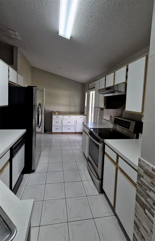 A kitchen features white cabinets, stainless steel appliances, and light-colored tile flooring — 2240 STONEHEDGE LOOP, KISSIMMEE, FL