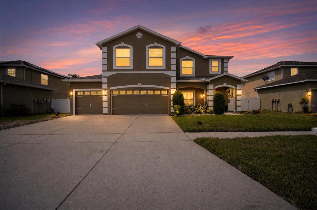 A two-story suburban house with a three-car garage at sunset — 12209 CITRUS LEAF DRIVE, GIBSONTON, FL