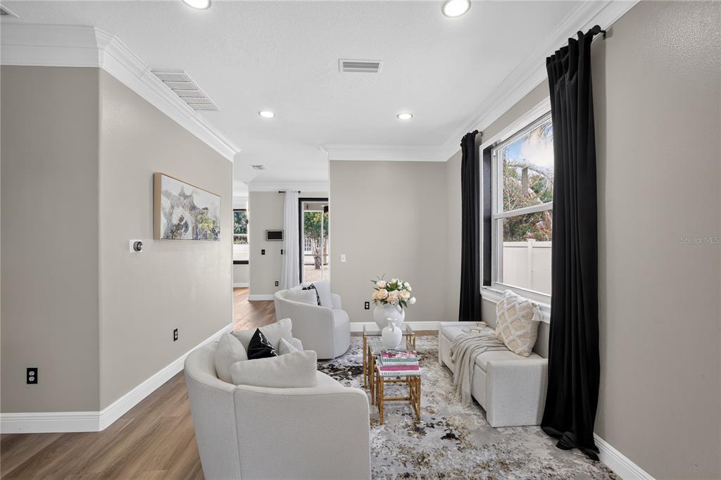 A bright living room features light-colored armchairs, a bench, a patterned rug, and dark curtains — 12209 CITRUS LEAF DRIVE, GIBSONTON, FL