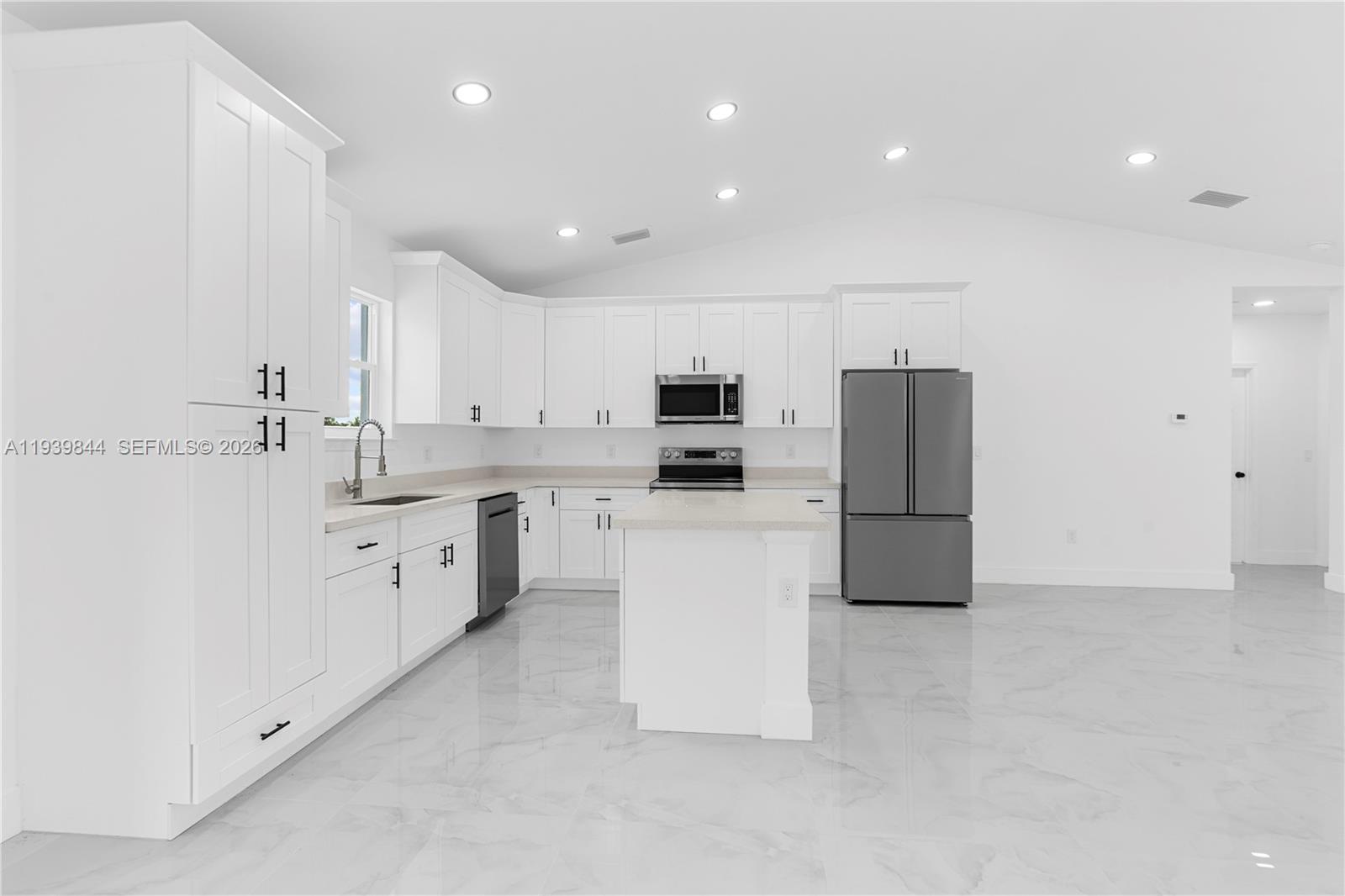 A modern kitchen features white cabinets, stainless steel appliances, a center island, and tiled floors — 3117 W 64th W, Lehigh Acres FL 33971, LEHIGH ACRES, FL