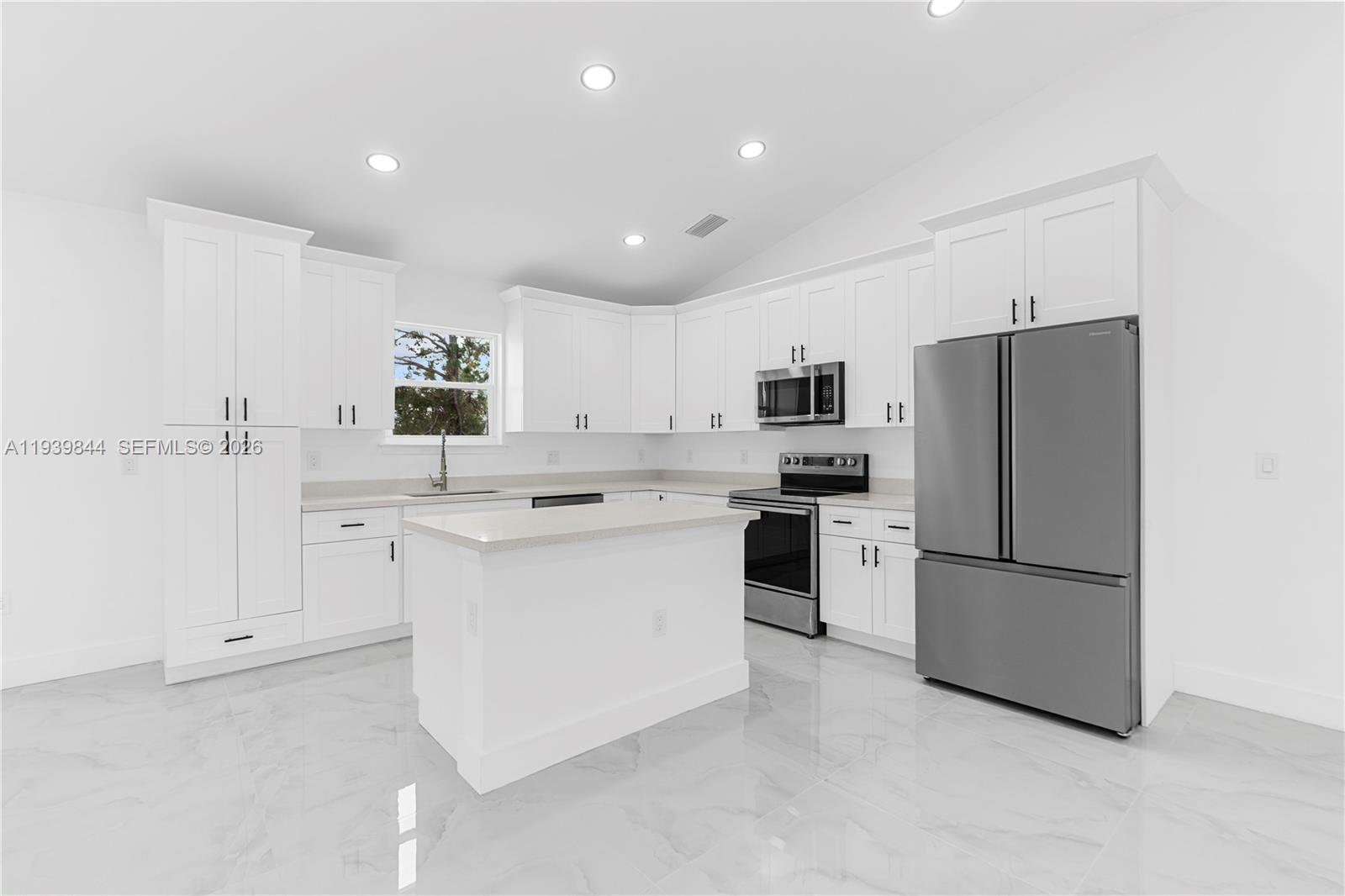 A modern kitchen features white cabinetry, stainless steel appliances, a center island, and tiled floors — 3117 W 64th W, Lehigh Acres FL 33971, LEHIGH ACRES, FL