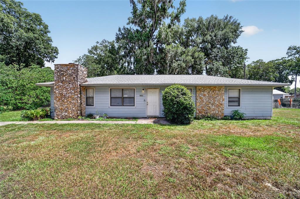 A single-story house with light gray siding, a stone chimney, and a stone accent wall — 945 NW 64TH PLACE, OCALA, FL