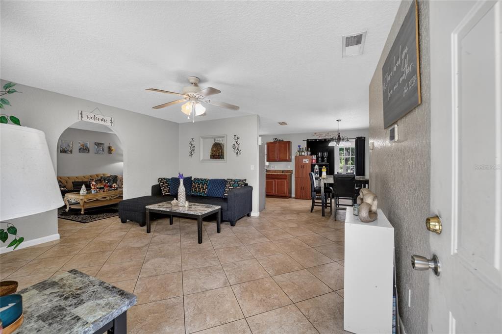 An open-concept living and dining area features tile flooring, a ceiling fan, and arched entryways — 945 NW 64TH PLACE, OCALA, FL