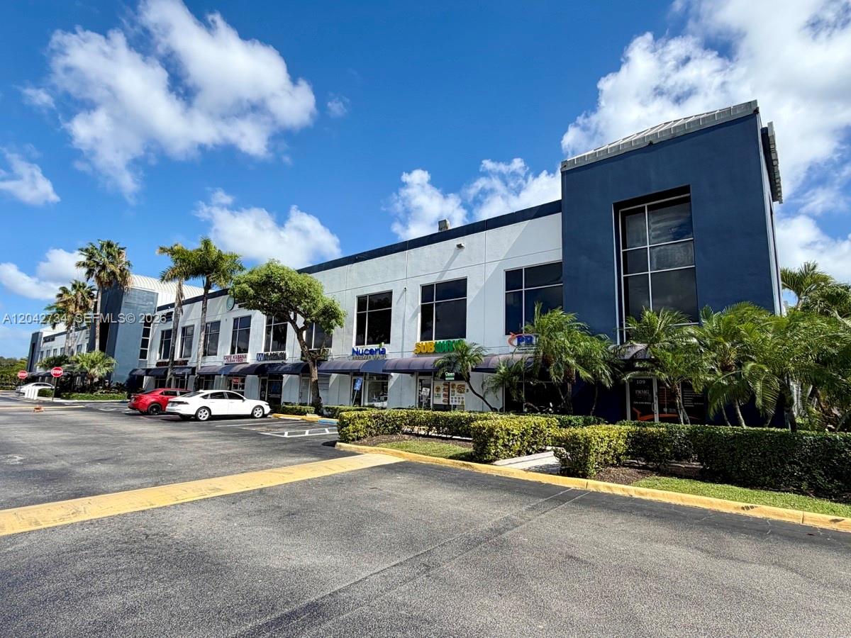 A two-story commercial building with a parking lot and palm trees under a blue sky — 7500 NW 25th St # 107, Miami FL 33122, MIAMI, FL