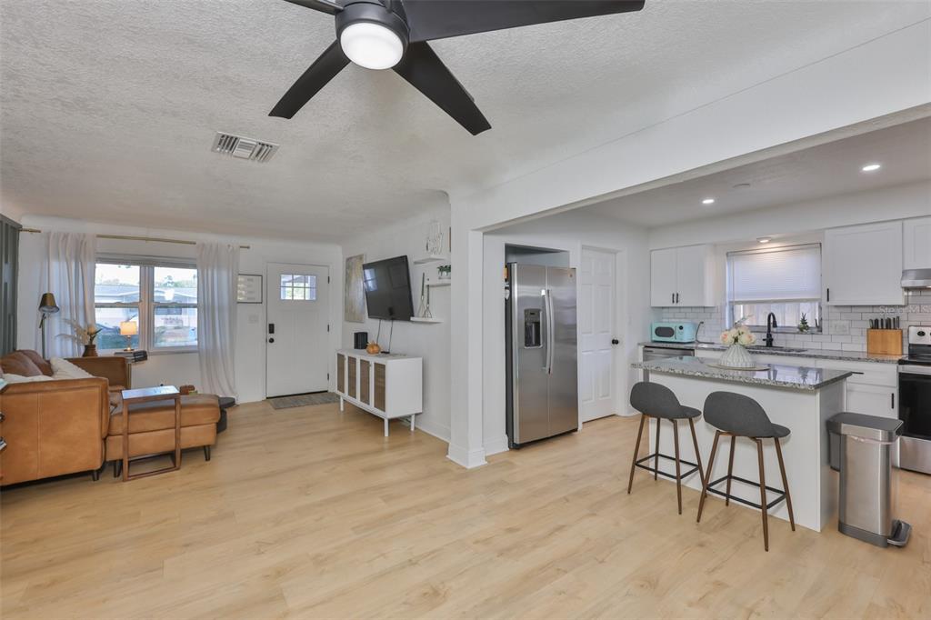 An open-concept living room and kitchen feature light wood flooring, white cabinetry, and a ceiling fan — 8391 59TH LANE N, PINELLAS PARK, FL
