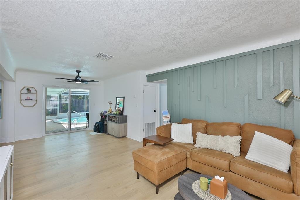A living room features light wood flooring, a tan sectional sofa, and a green accent wall — 8391 59TH LANE N, PINELLAS PARK, FL