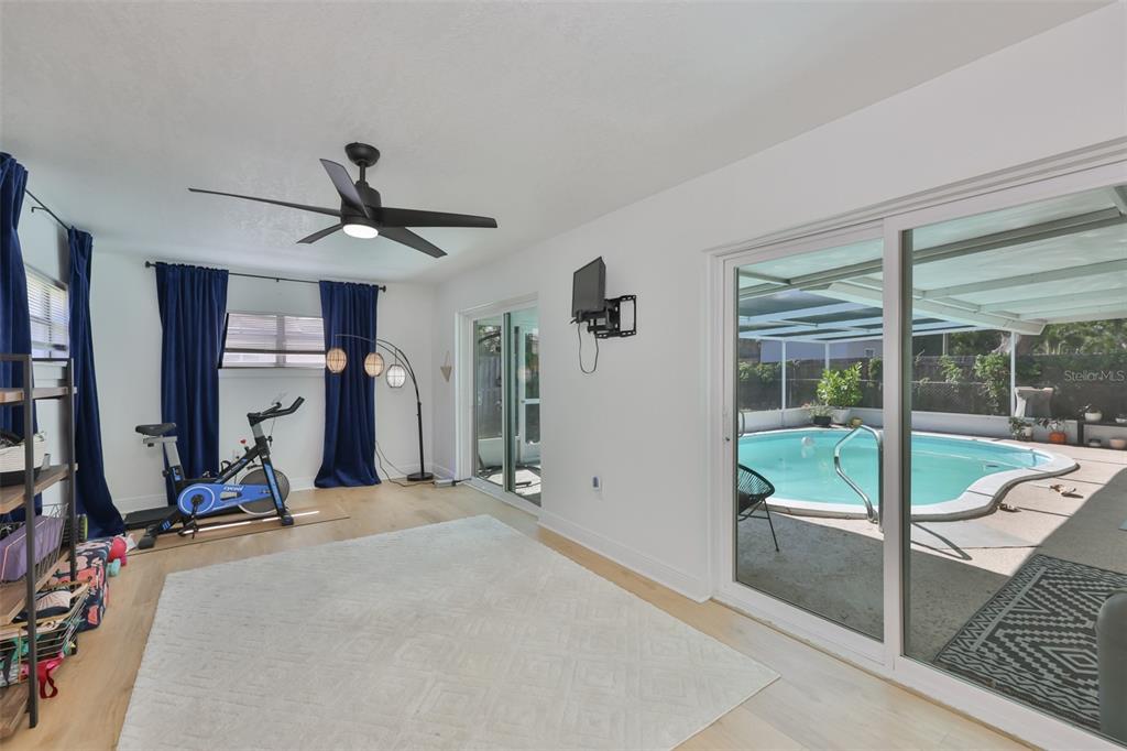 A room with light wood floors, a stationary bike, and sliding doors overlooking a pool — 8391 59TH LANE N, PINELLAS PARK, FL