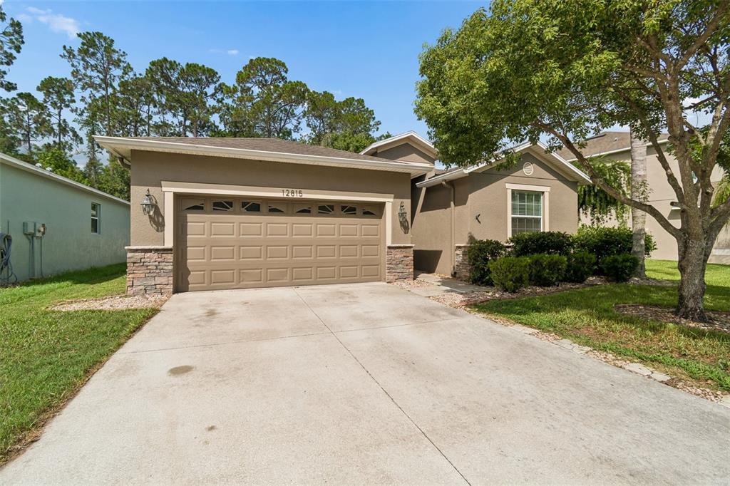 A single-story house with a tan stucco exterior, stone accents, and a two-car garage — 12815 WHITE BLUFF ROAD, HUDSON, FL