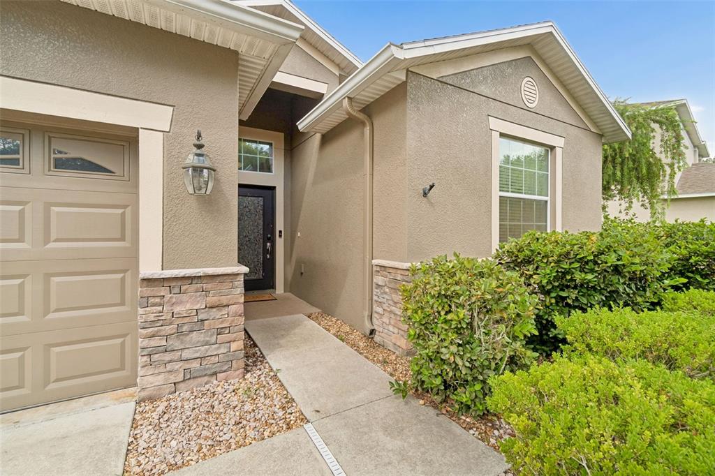 The exterior of a house features a tan stucco facade, stone accents, and a front entrance — 12815 WHITE BLUFF ROAD, HUDSON, FL