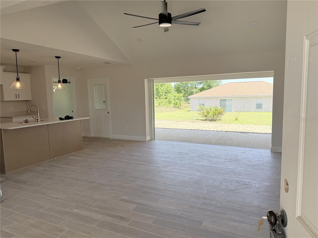 An open-concept living area features light wood-look tile flooring, a kitchen island, and sliding doors — 133 LARCH ROAD, OCALA, FL