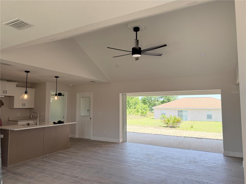 An open-concept kitchen and living area features a vaulted ceiling, ceiling fan, and sliding doors — 133 LARCH ROAD, OCALA, FL